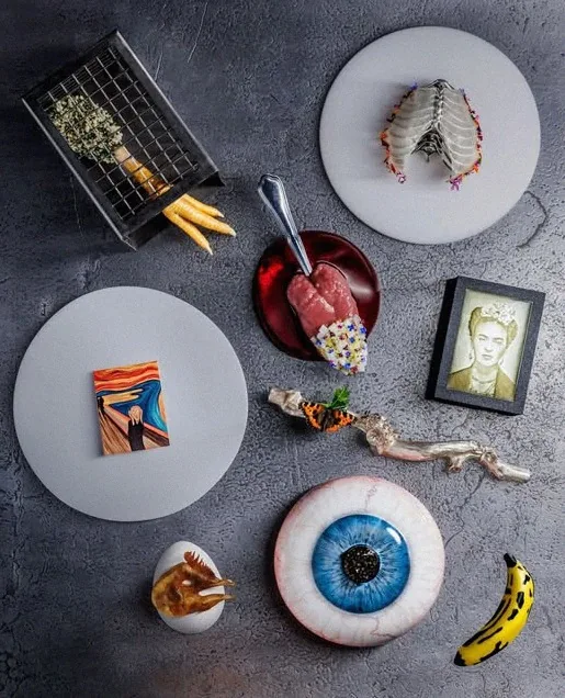 An overhead flatlay of Alchemist impressions: a Scream miniature, an eyeball, a banana, chicken feet and a Frida Kahlo portrait