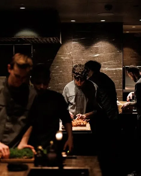 Alchemist chefs working under spotlights at the open pass